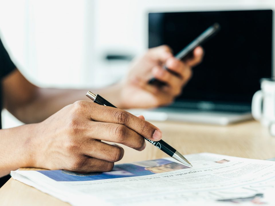 Une personne lit un journal en tenant un stylo à la main