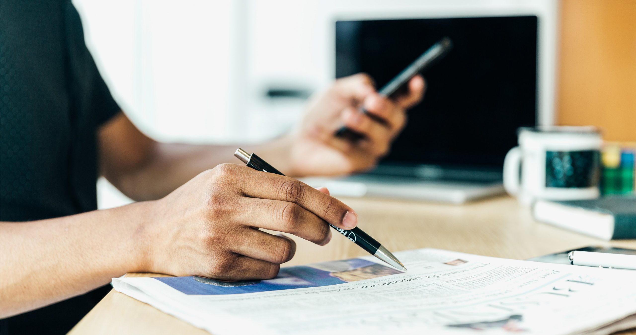 Une personne lit un journal en tenant un stylo à la main